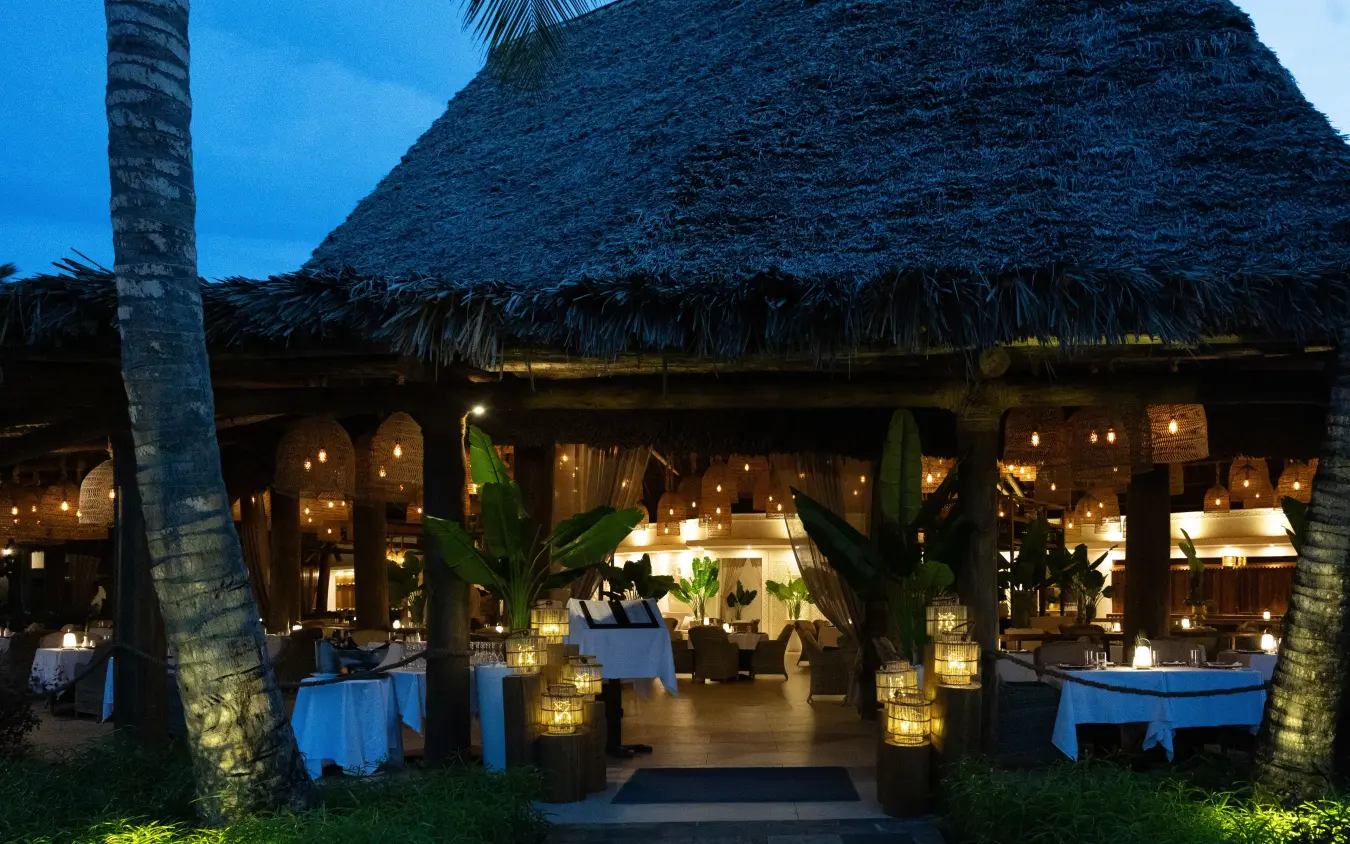 Thatched-roof dining pavilion lit at dusk with blue tablecloths and lanterns, Breezes Beach Club & Spa, Zanzibar & Pemba, Tanzania