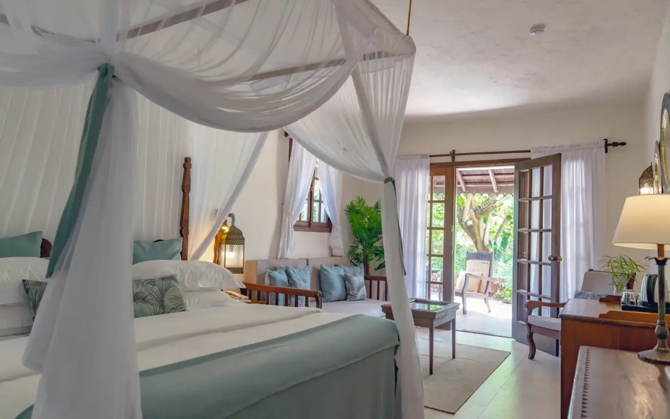 Luxury bedroom suite with four-poster canopy bed and terrace doors opening to gardens, Breezes Beach Club & Spa, Zanzibar & Pemba, Tanzania