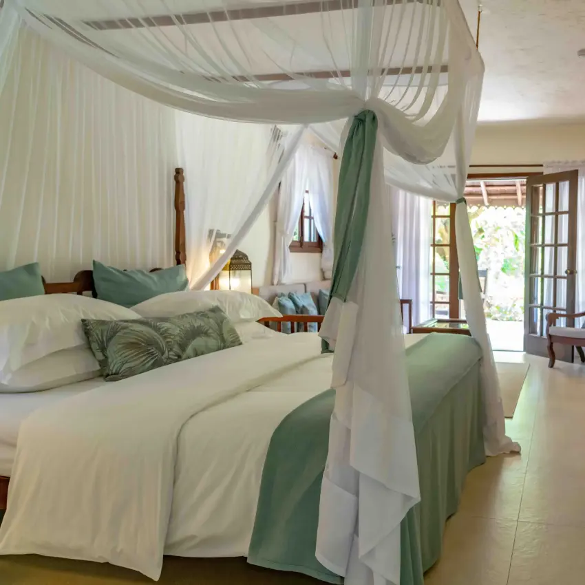 Luxury bedroom with four-poster canopy bed and French doors opening to gardens, Breezes Beach Club & Spa, Zanzibar & Pemba, Tanzania