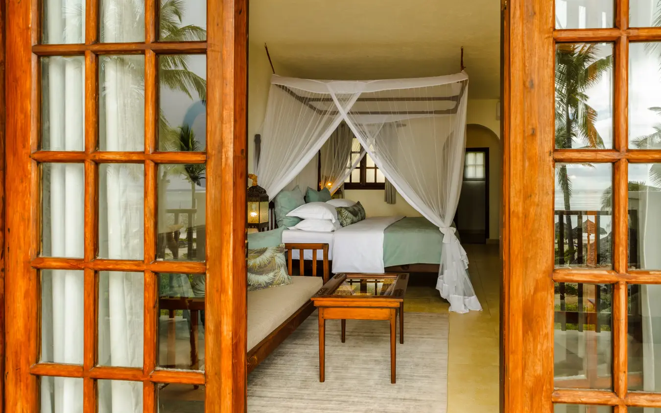 Luxury bedroom with sheer canopy bed and wooden french doors, Breezes Beach Club & Spa, Zanzibar & Pemba, Tanzania