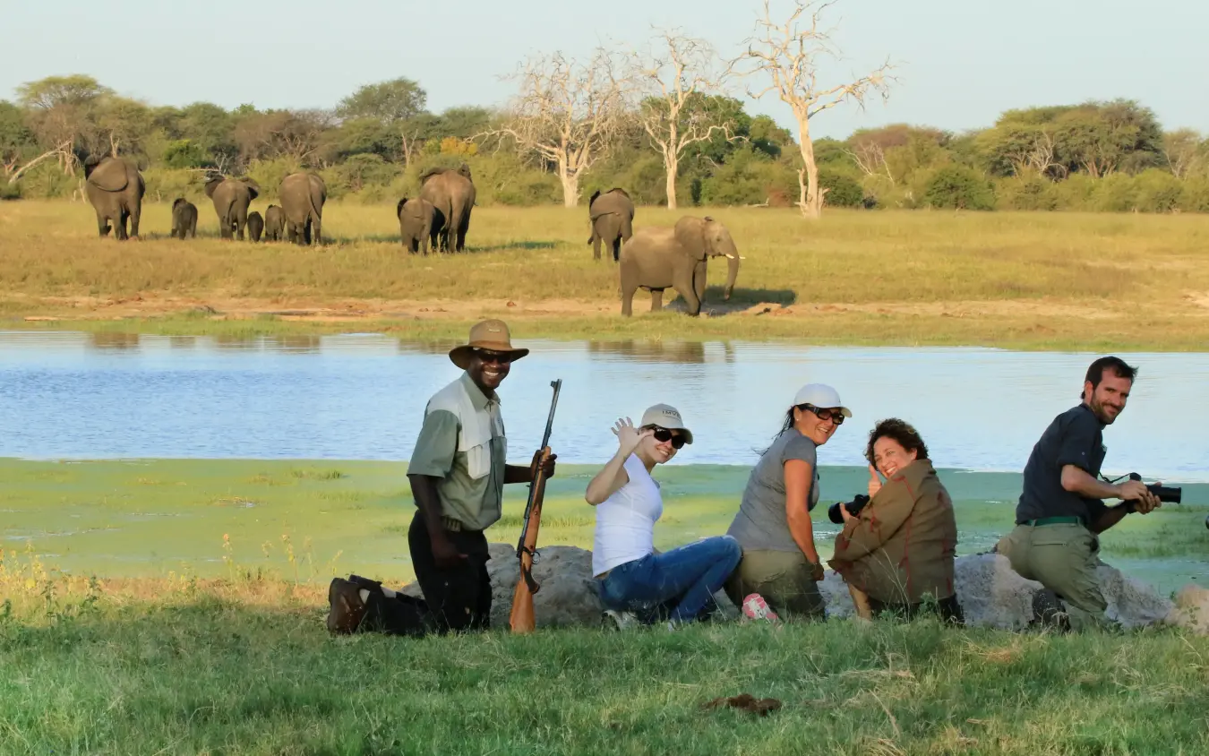 Park ranger with visitors observing elephants at waterhole at dusk, Camelthorn Lodge, Hwange National Park, Zimbabwe