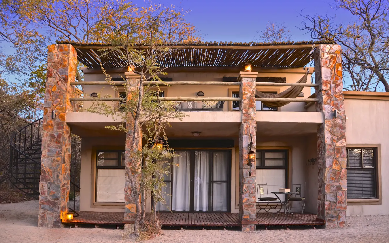 Modern lodge accommodation with stone pillars and wooden pergola at dusk, Camelthorn Lodge, Hwange National Park, Zimbabwe
