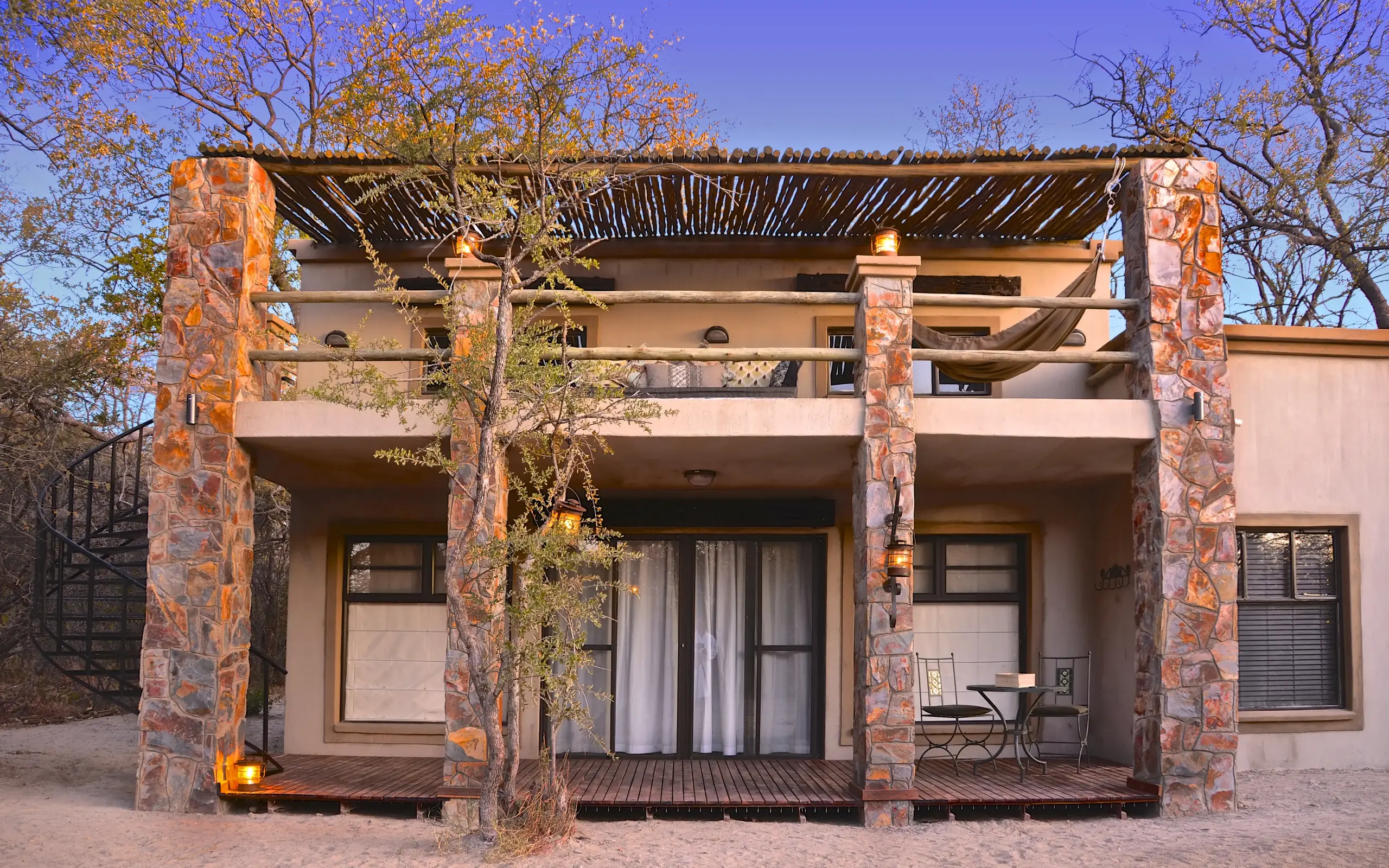 Modern lodge accommodation with stone pillars and wooden pergola at dusk, Camelthorn Lodge, Hwange National Park, Zimbabwe