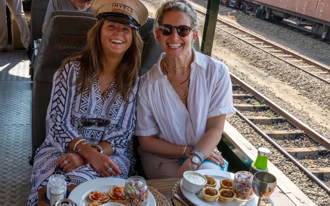 Guests enjoying meal on vintage train carriage beside railway tracks, Camelthorn Lodge, Hwange National Park, Zimbabwe