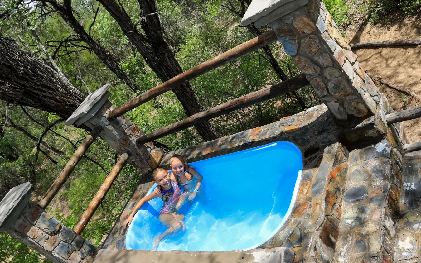 Woman and child in swimming pool surrounded by natural stone walls and forest, Camelthorn Lodge, Hwange National Park, Zimbabwe