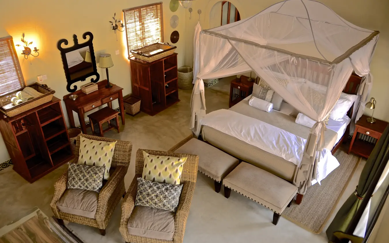 Luxury bedroom with four-poster canopy bed and woven seating area, Camelthorn Lodge, Hwange National Park, Zimbabwe
