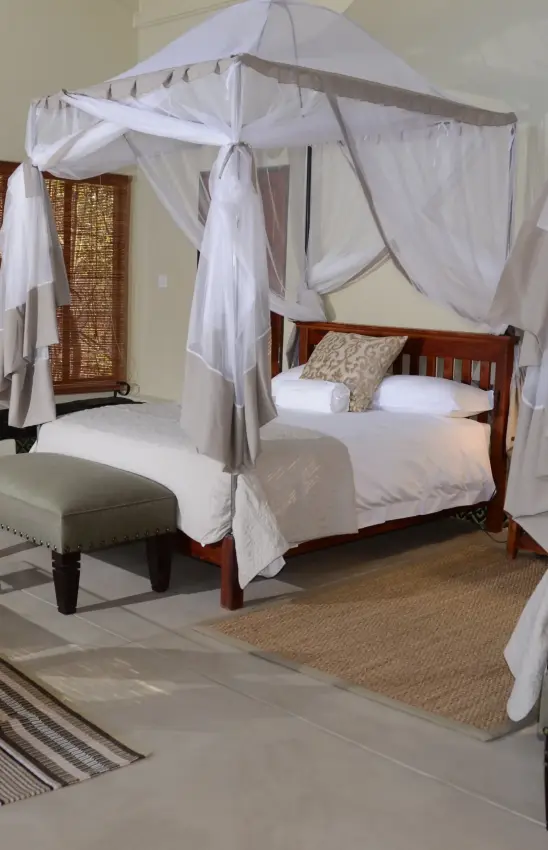 Four-poster bed with white sheer canopy in luxury bedroom suite, Camelthorn Lodge, Hwange National Park, Zimbabwe