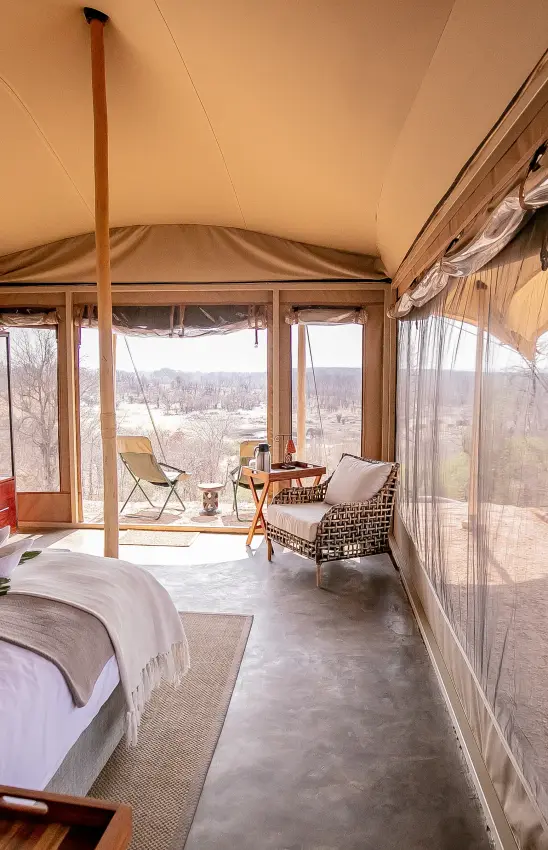 Glamping tent interior with bed and lounge area overlooking bare landscape, Camp Chitubu, Hwange National Park, Zimbabwe