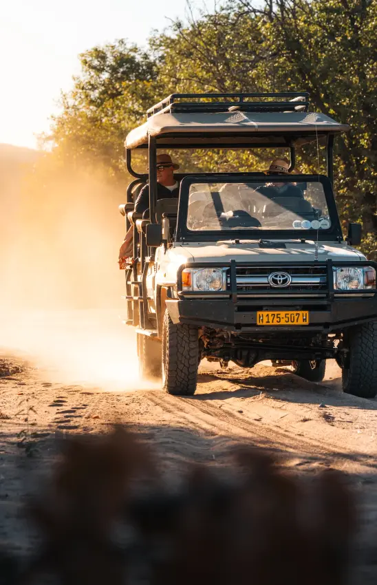 Safari truck driving on dusty road with passengers on open-air platform, Camp Doros, Damaraland, Namibia