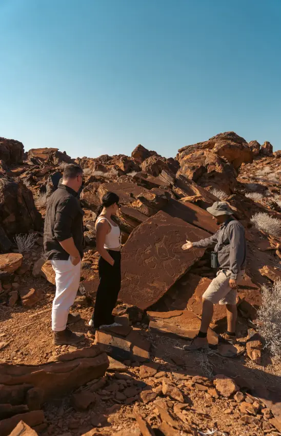 Group viewing ancient rock petroglyphs in desert landscape, Camp Doros, Damaraland, Namibia