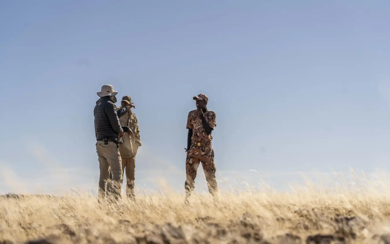 Guides and guests standing in dry grassland under clear sky, Camp Doros, Damaraland, Namibia