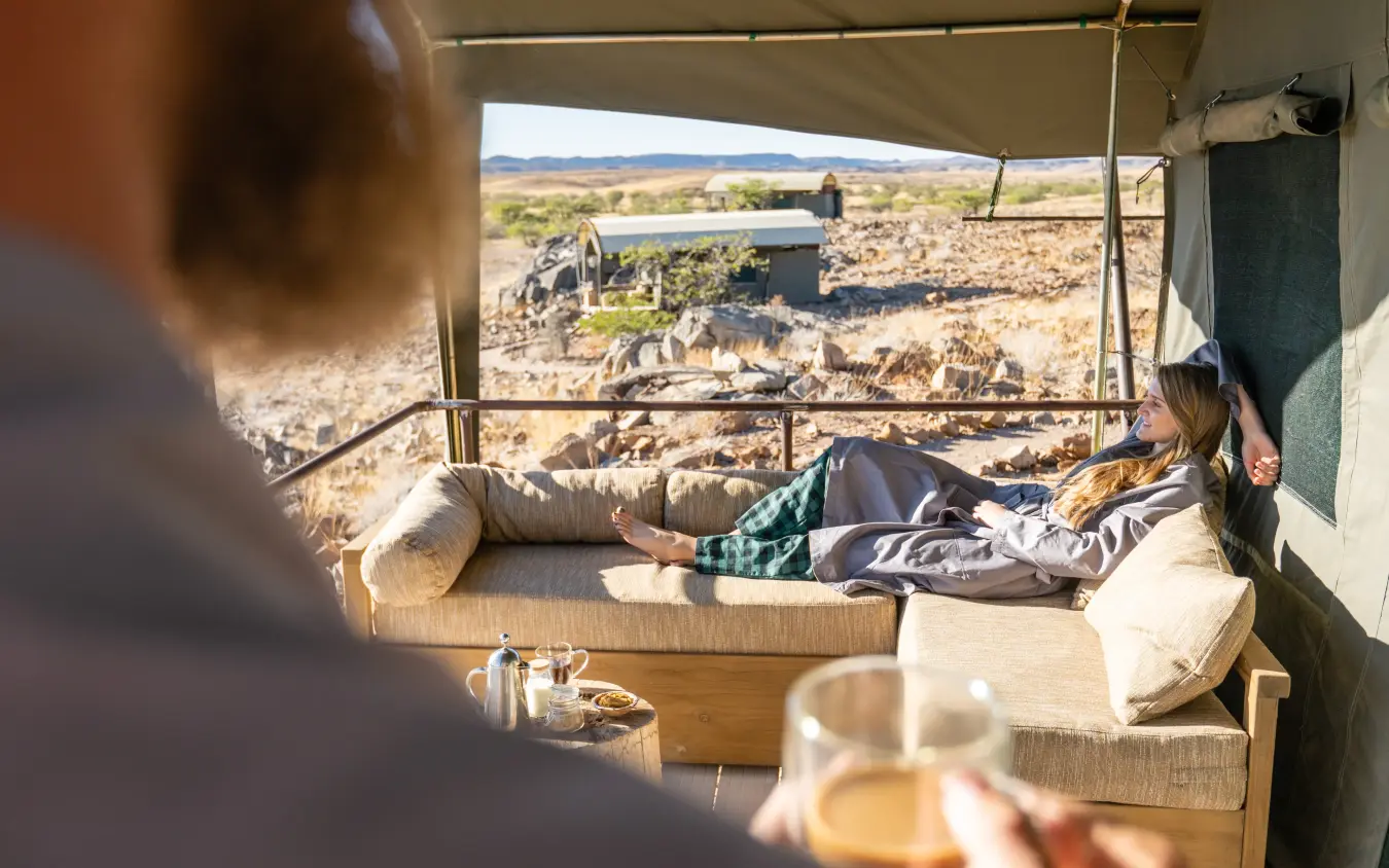 Guests relaxing in safari lodge tent with savanna landscape view, Camp Doros, Damaraland, Namibia