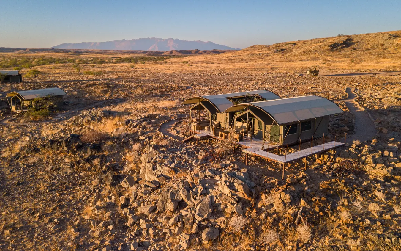 Glamping tents with shade structures on rocky desert terrain at sunset, Camp Doros, Damaraland, Namibia
