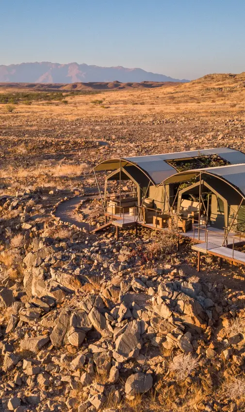 Glamping tents with shade structures on rocky desert terrain at sunset, Camp Doros, Damaraland, Namibia