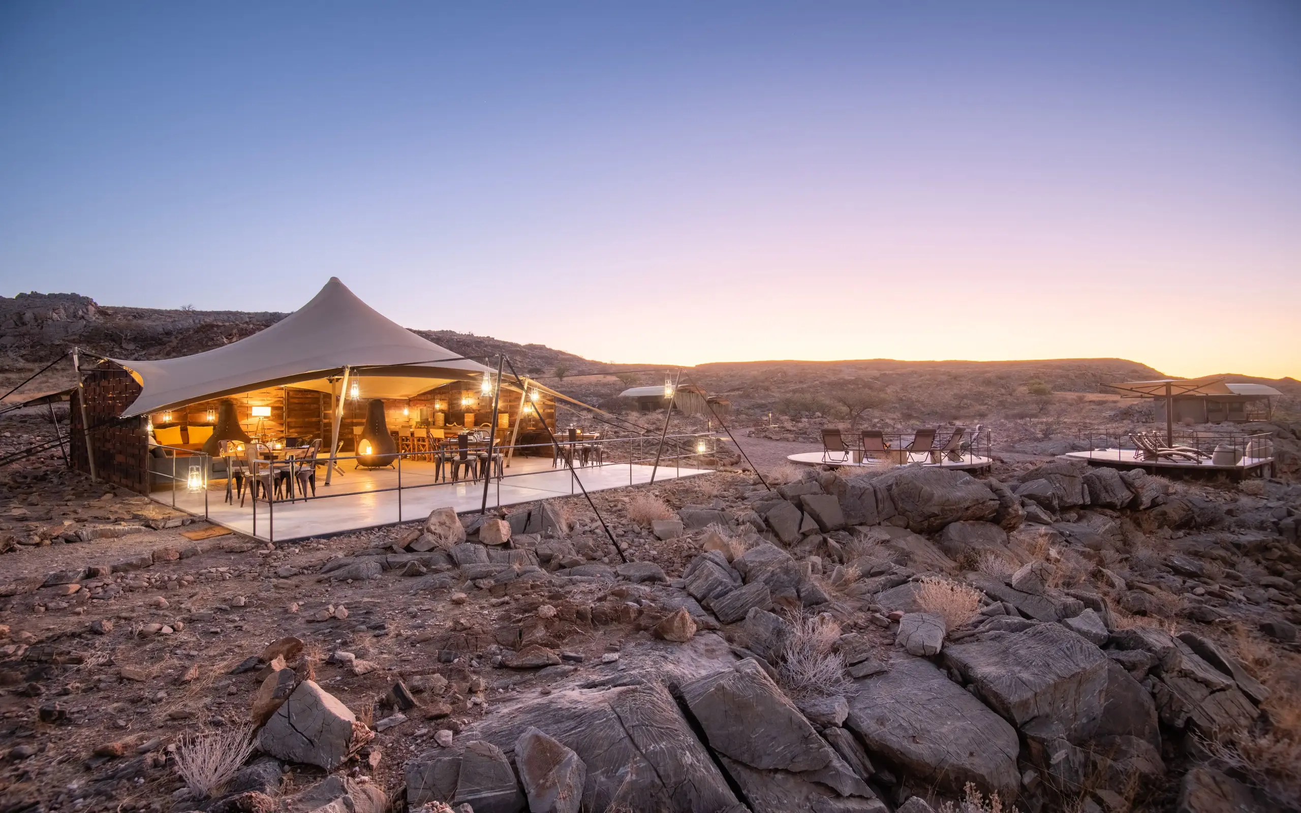 Luxury tent with warm lighting on rocky desert landscape at dusk, Camp Doros, Damaraland, Namibia