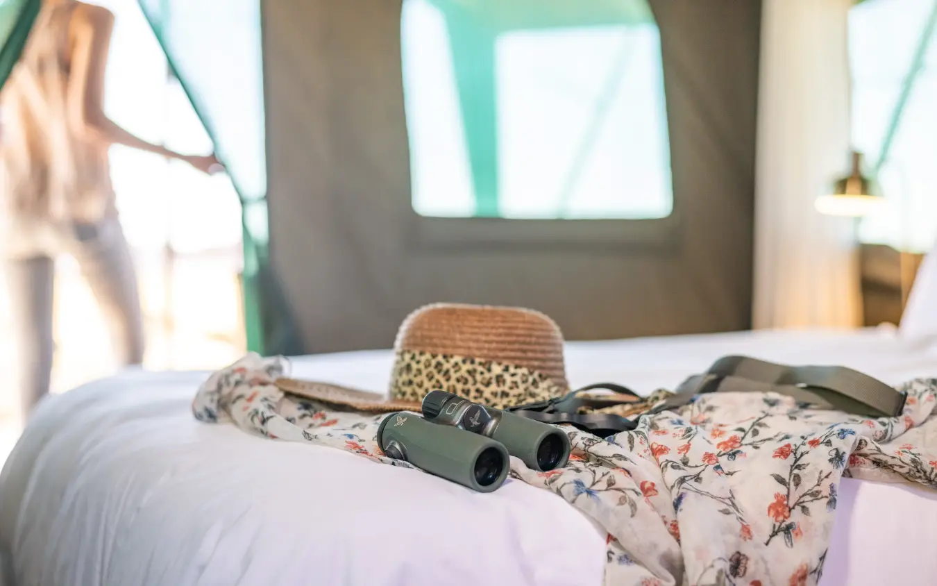 Binoculars and safari gear laid on bed in canvas glamping tent, Camp Doros, Damaraland, Namibia