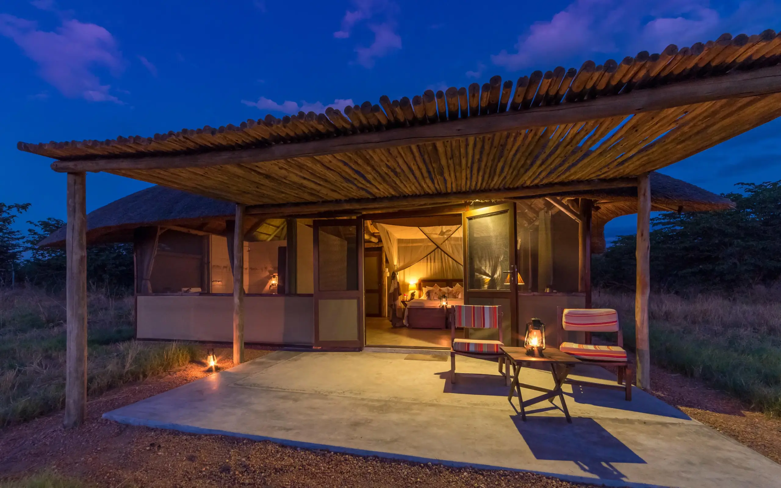 Illuminated safari lodge with wooden pergola at dusk, Camp Hwange, Hwange National Park, Zimbabwe