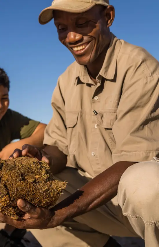 Guide showing soil sample to two young guests outdoors, Camp Kipwe, Damaraland, Namibia