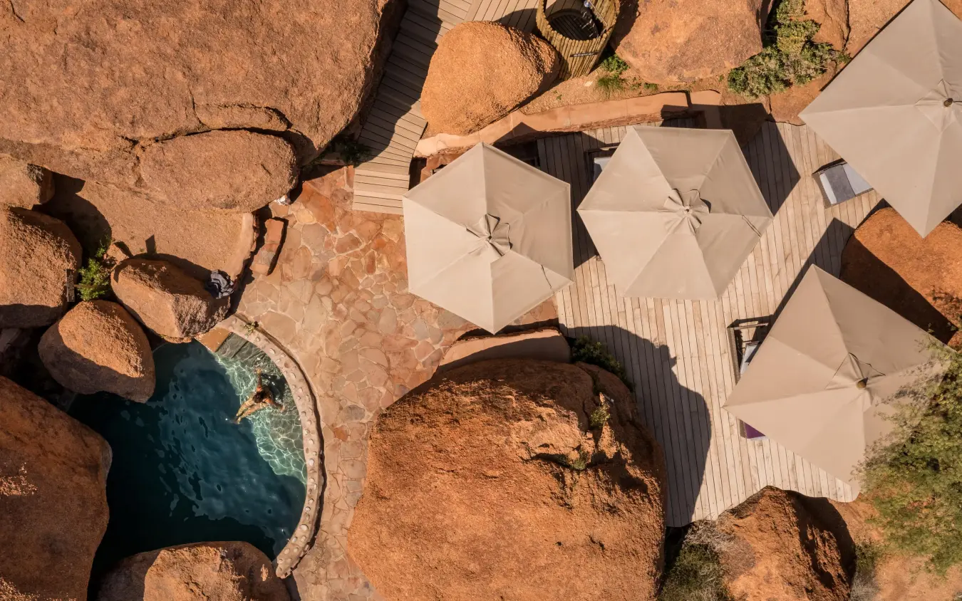 Overhead view of luxury camp with cream umbrellas and rocky terrain, Camp Kipwe, Damaraland, Namibia
