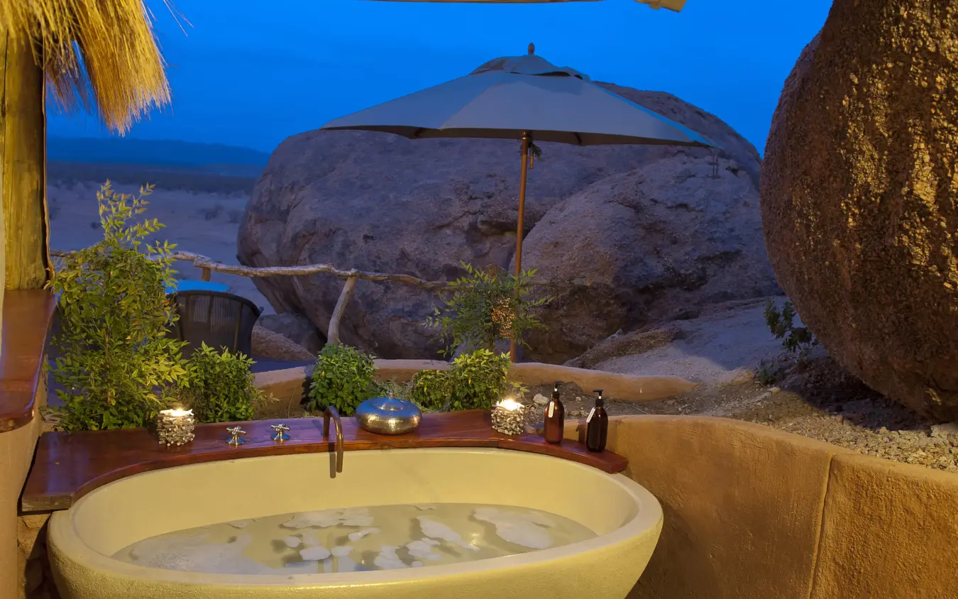 Outdoor bathtub at dusk with desert rock formations, Camp Kipwe, Damaraland, Namibia
