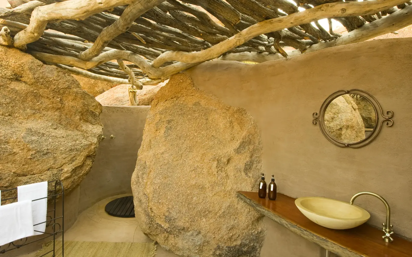 Bathroom interior with natural stone boulder and wooden beam ceiling, Camp Kipwe, Damaraland, Namibia