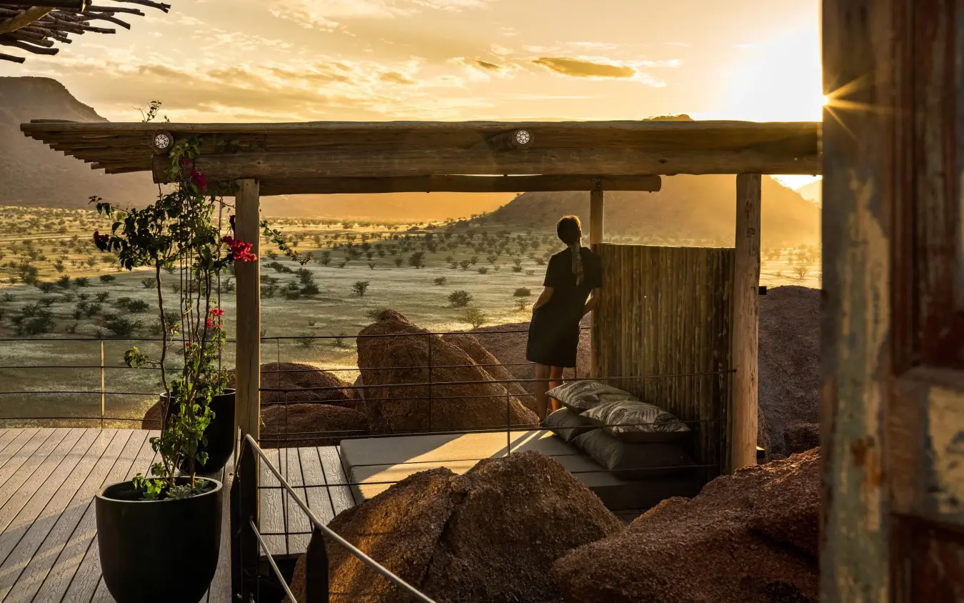 Person standing on wooden deck overlooking vast savanna landscape, Camp Kipwe, Damaraland, Namibia
