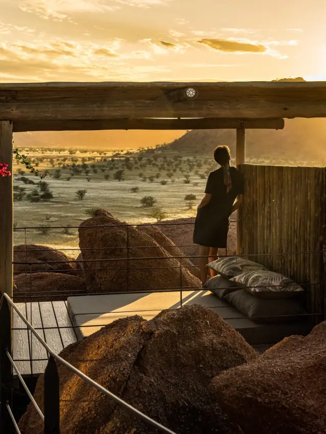 Person standing on wooden deck overlooking vast savanna landscape, Camp Kipwe, Damaraland, Namibia