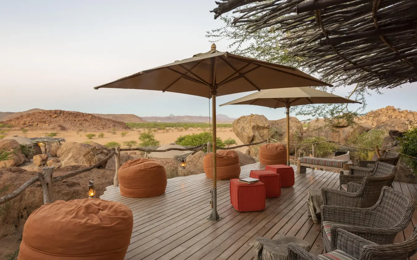 Wooden deck with umbrellas overlooking arid savanna landscape, Camp Kipwe, Damaraland, Namibia