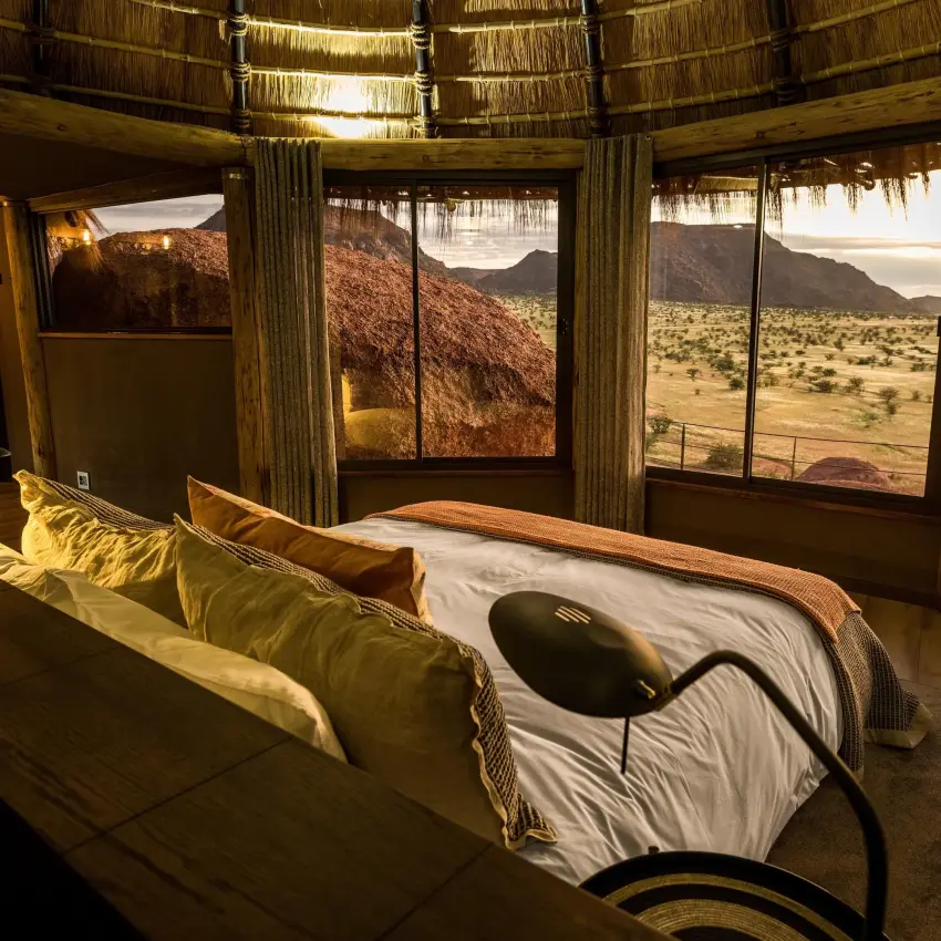 Bedroom with large windows overlooking arid savanna landscape, Camp Kipwe, Damaraland, Namibia