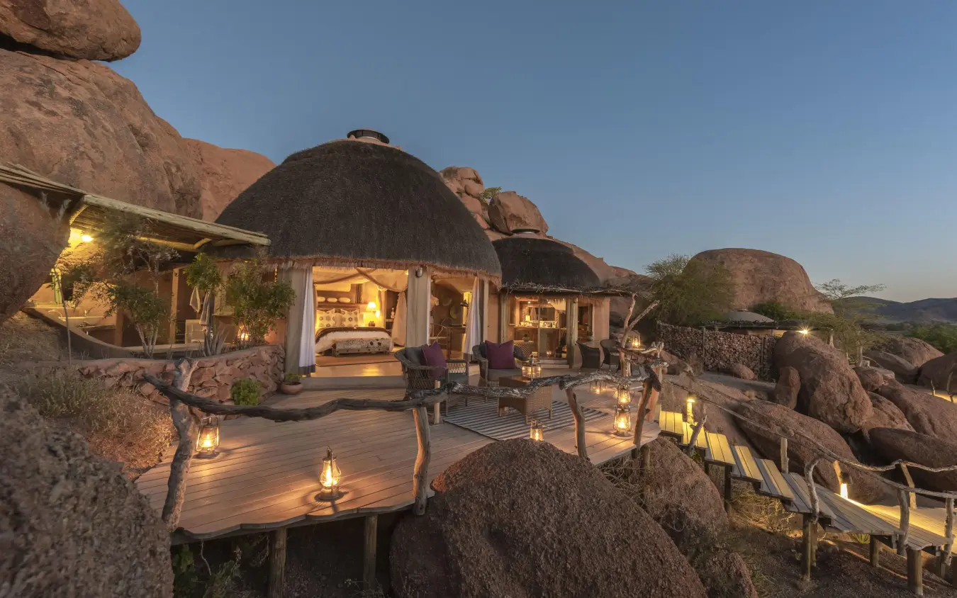 Thatched-roof lodge nestled among massive boulders at dusk, Camp Kipwe, Damaraland, Namibia