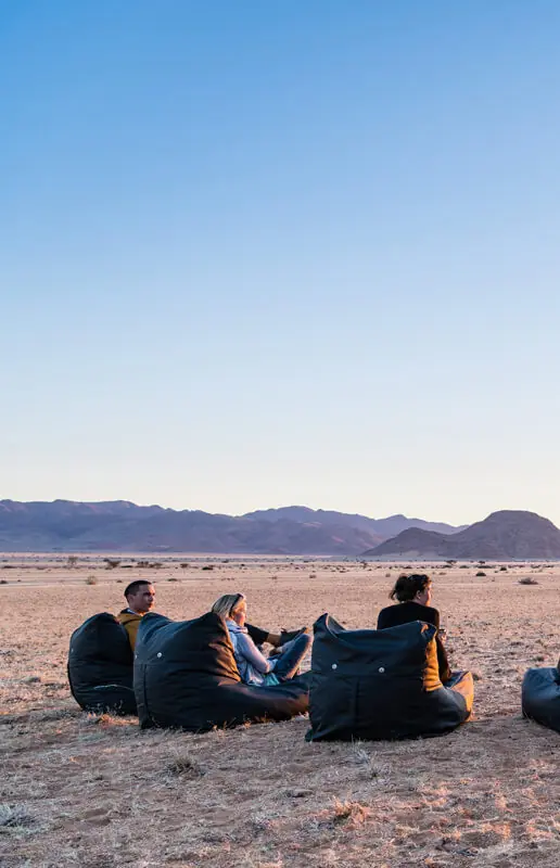 Guests relaxing on bean bags in desert landscape at sunset, Camp Sossus, Sossusvlei, Namibia