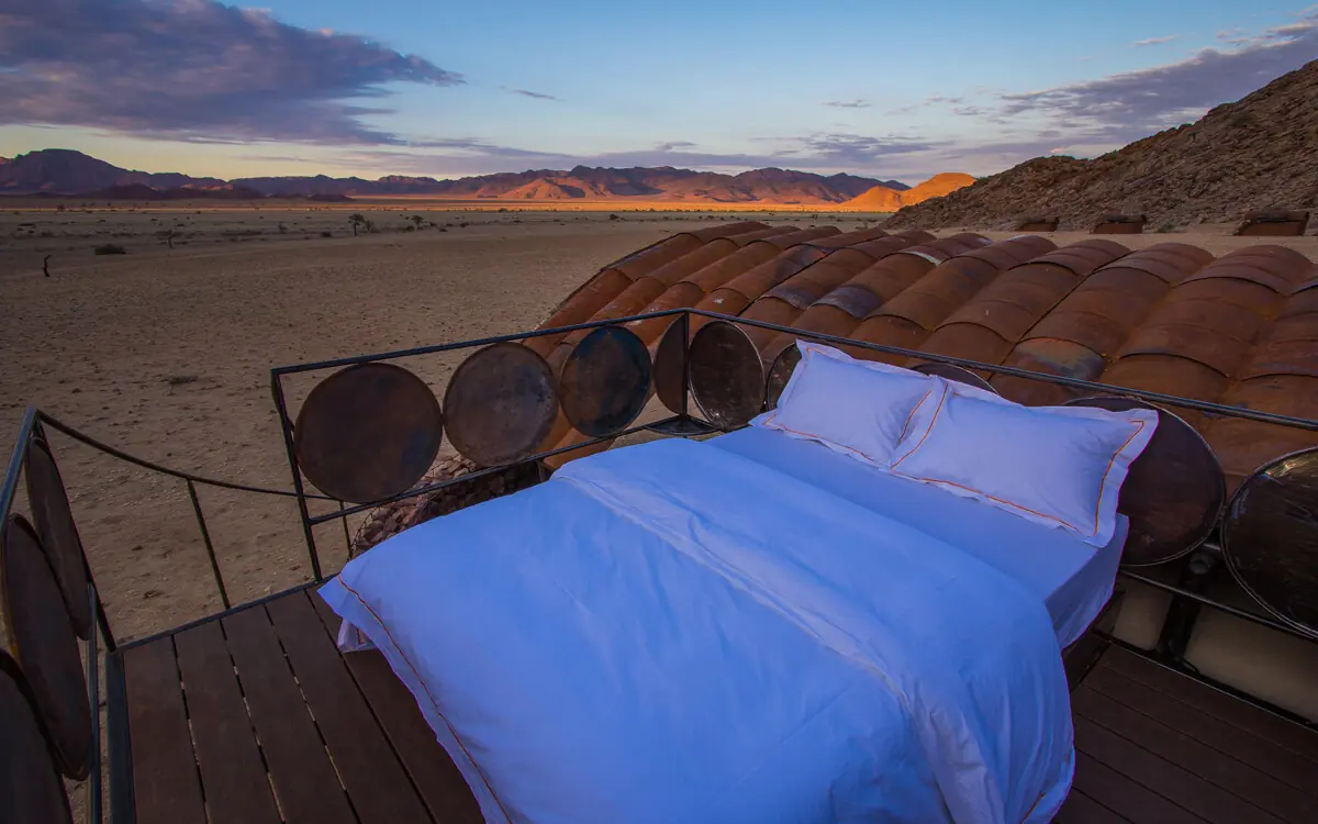 Bed on desert platform overlooking mountains at sunset, Camp Sossus, Sossusvlei, Namibia