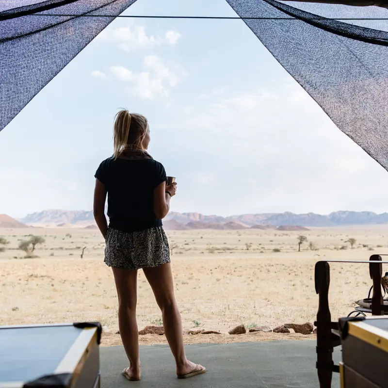 Guest standing on tent deck viewing vast desert landscape, Camp Sossus, Sossusvlei, Namibia