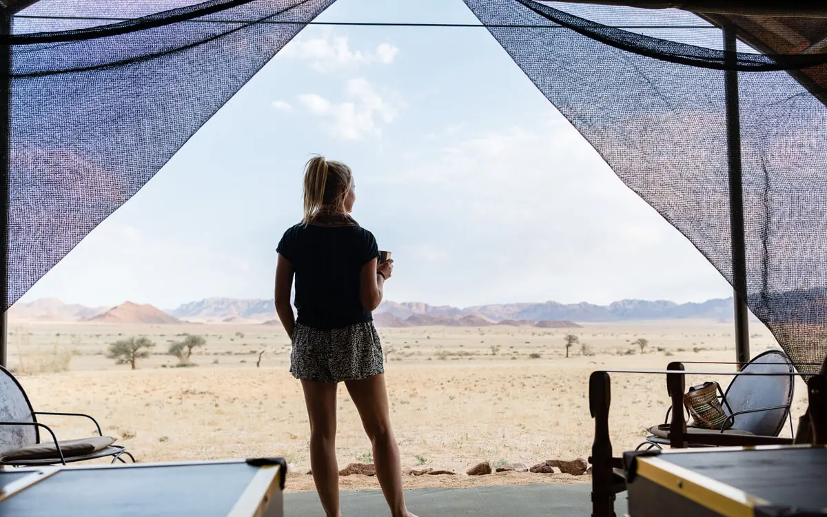 Guest standing on tent deck viewing vast desert landscape, Camp Sossus, Sossusvlei, Namibia