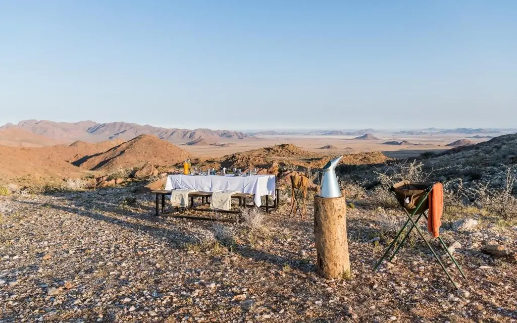 Desert dining setup with white tablecloth and mountain views, Camp Sossus, Sossusvlei, Namibia