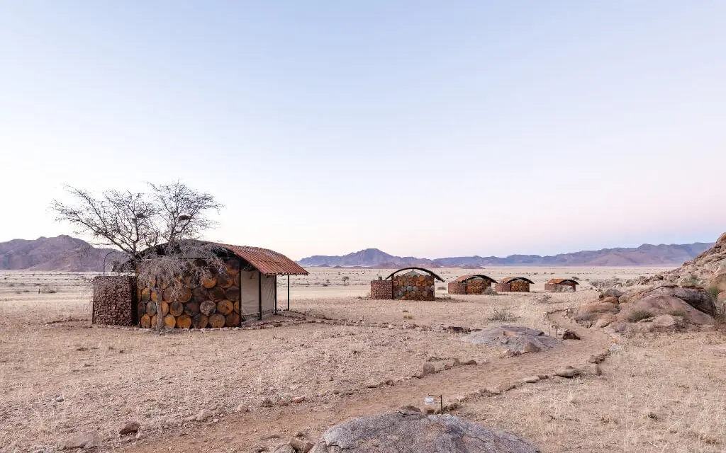 Desert camp structures with acacia tree and mountains, Camp Sossus, Sossusvlei, Namibia