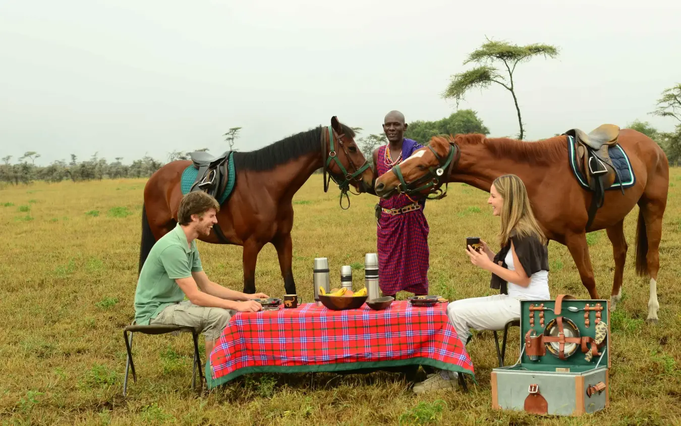 Guests dining outdoors with horses and Maasai guide, Campi ya Kanzi, Amboseli and Chyulu Hills, Kenya