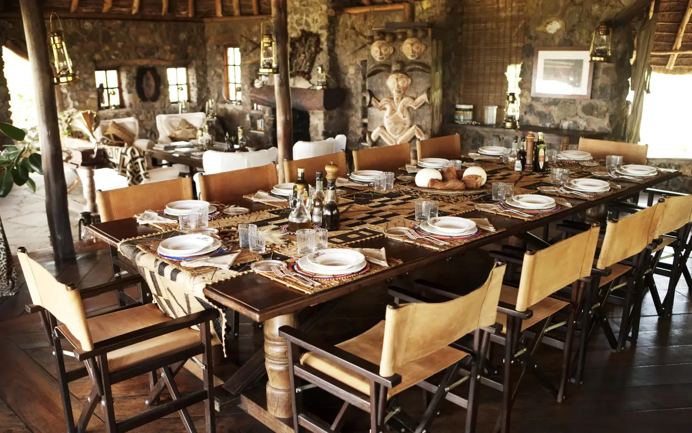 Long dining table set for multiple guests in rustic interior, Campi ya Kanzi, Amboseli and Chyulu Hills, Kenya