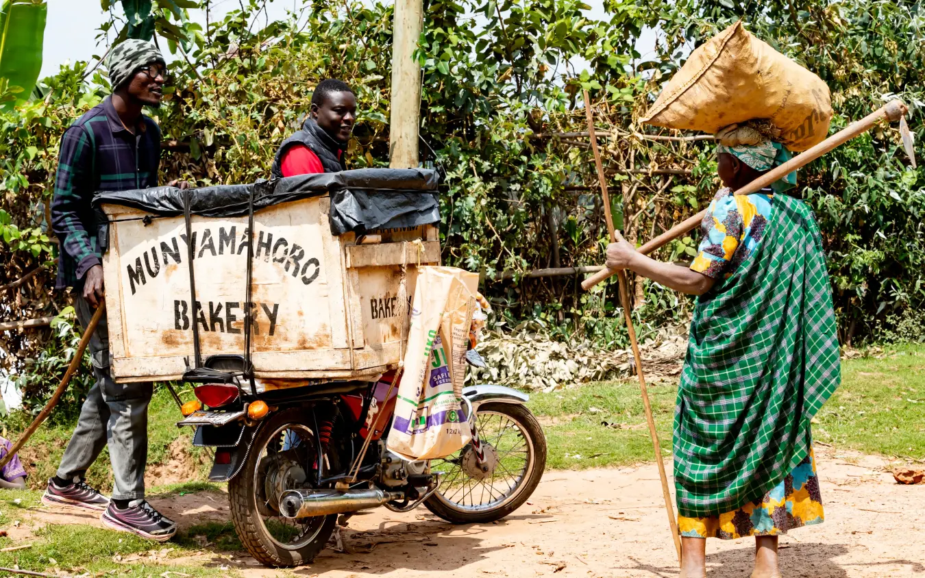 Local woman interacting with bakery delivery workers outdoors, Chameleon Hill Lodge, Lake Mutanda, Uganda
