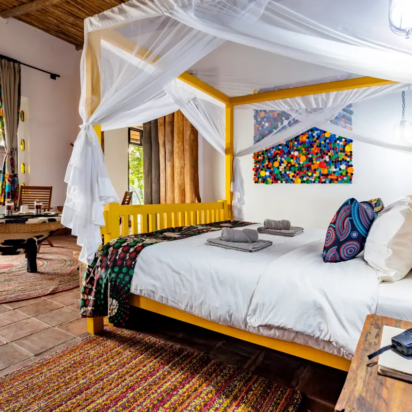 Canopied bed with yellow frame and white drapes in bedroom, Chameleon Hill Lodge, Lake Mutanda, Uganda