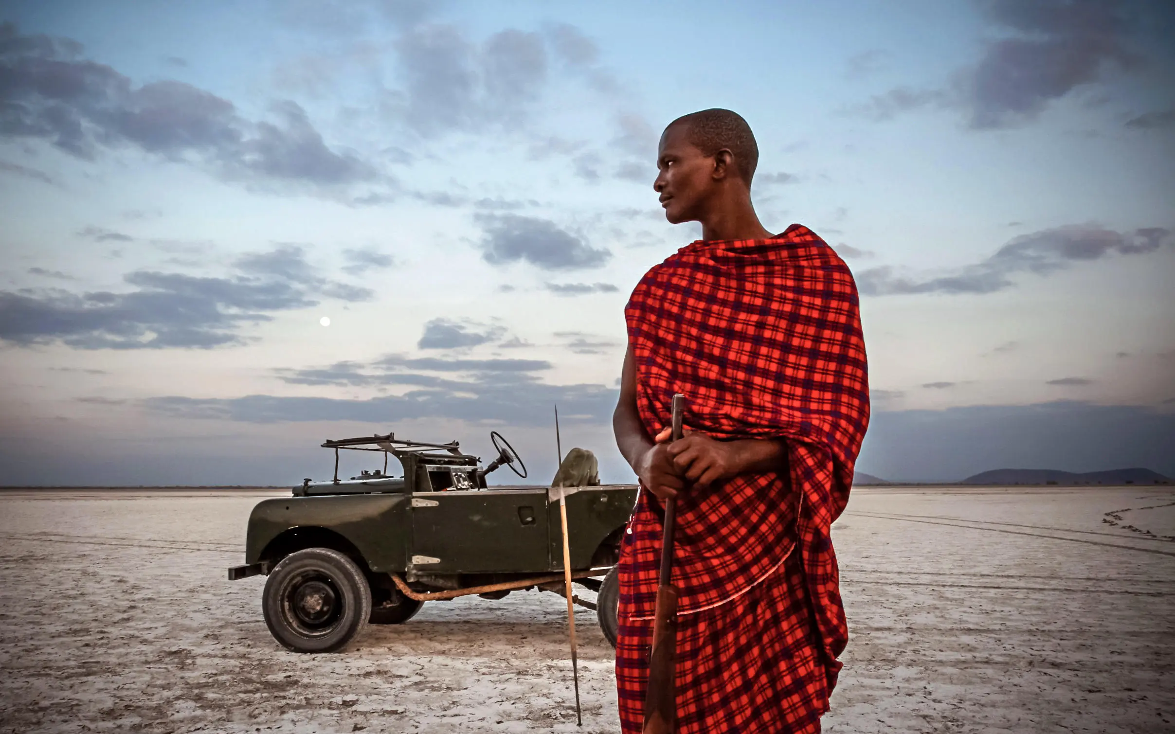 Maasai guide standing by vintage safari vehicle at sunset, Lake Manyara, Tanzania