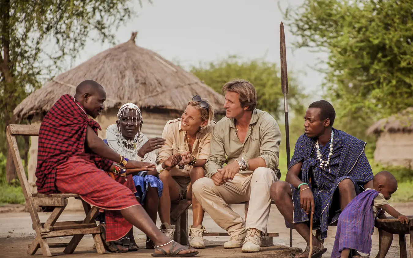 Guests meeting with local community members outside traditional thatched village hut, Chem Chem Lodge, Lake Manyara, Tanzania