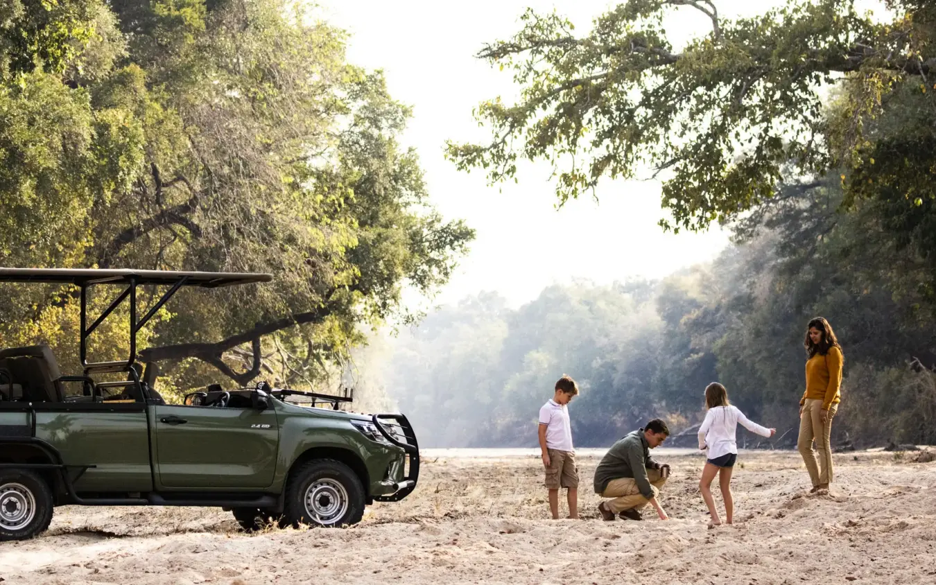Family exploring sandy riverbank near safari vehicle, Chikwenya Camp, Mana Pools, Zimbabwe