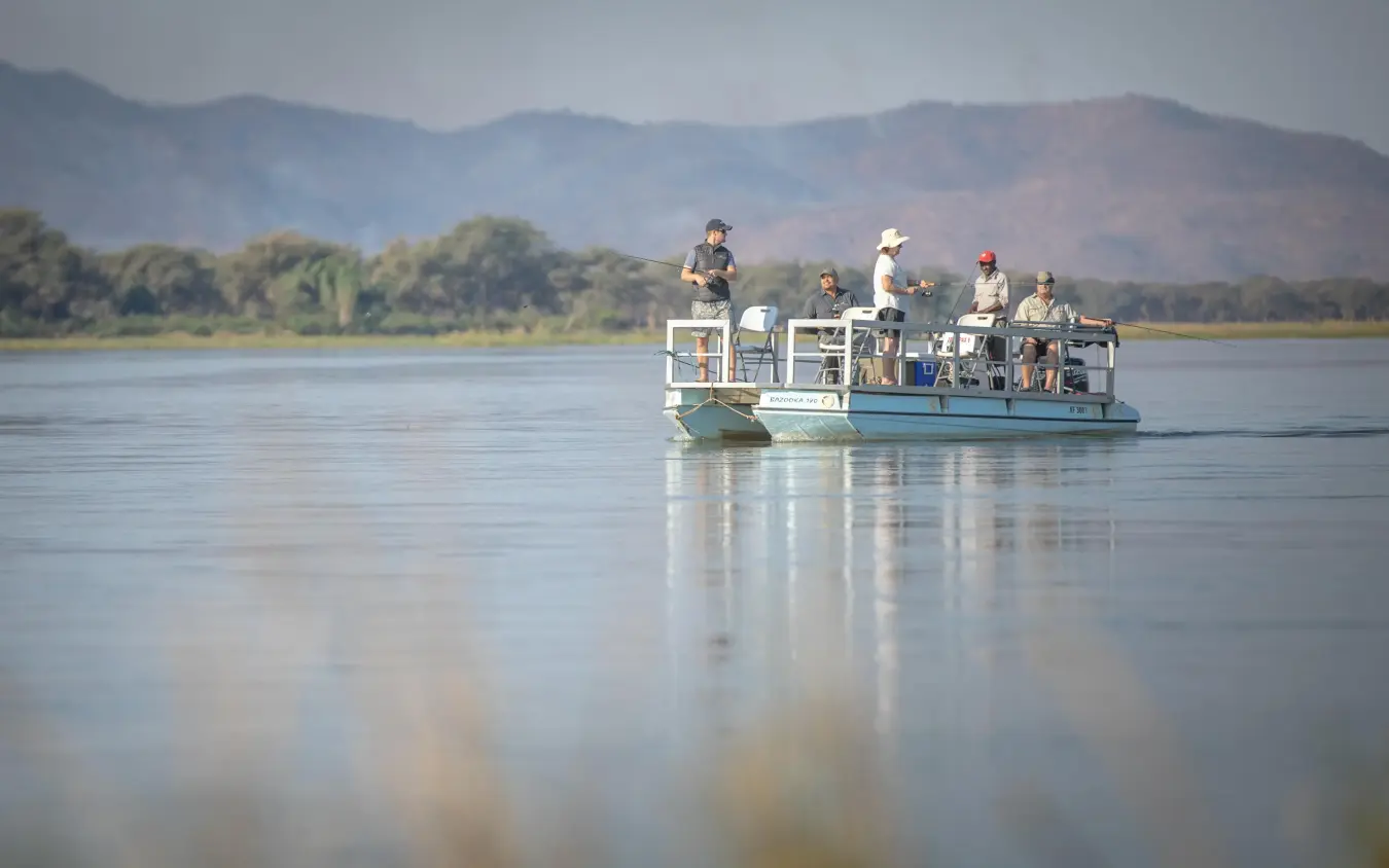 Guests on boat safari on calm river with mountains, Chikwenya Camp, Mana Pools, Zimbabwe
