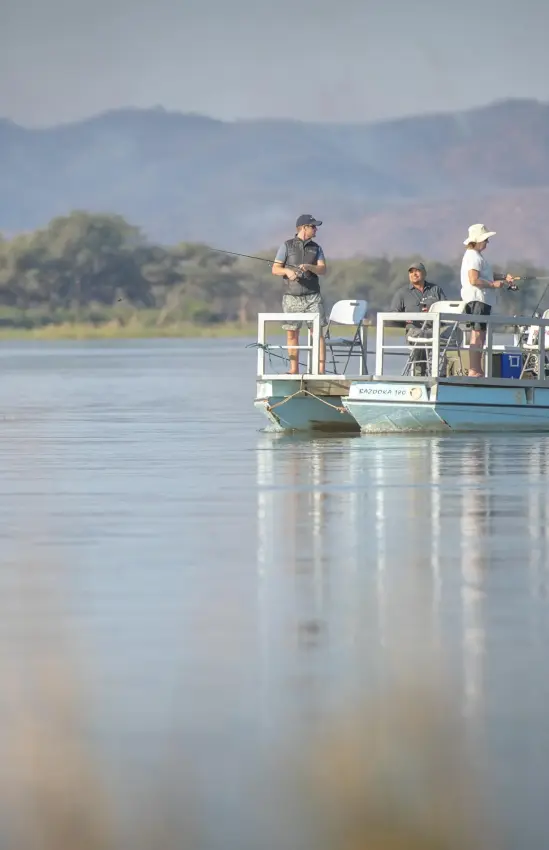 Guests on boat safari on calm river with mountains, Chikwenya Camp, Mana Pools, Zimbabwe
