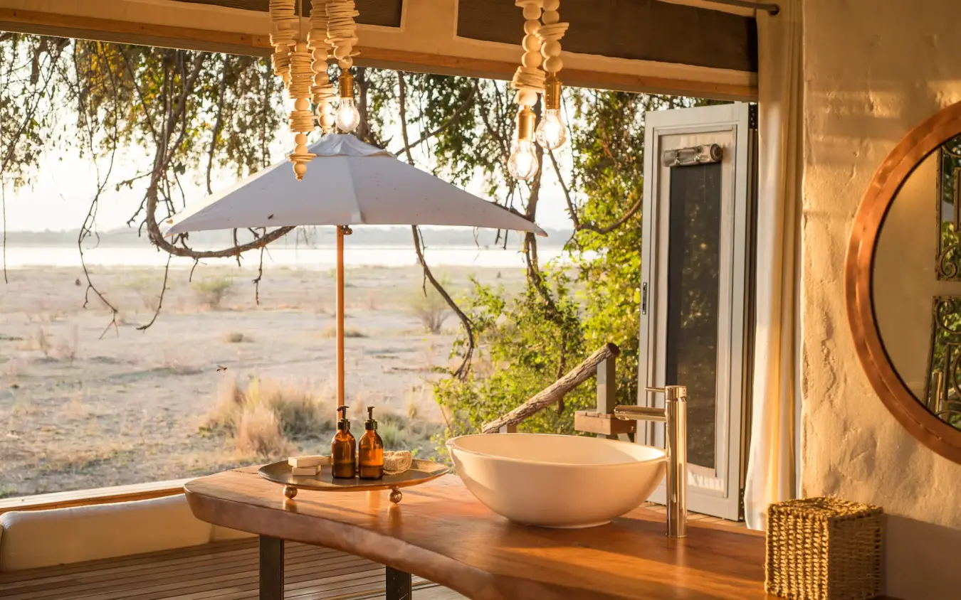 Outdoor wooden deck with basin sink and umbrella overlooking savanna, Chikwenya Camp, Mana Pools, Zimbabwe
