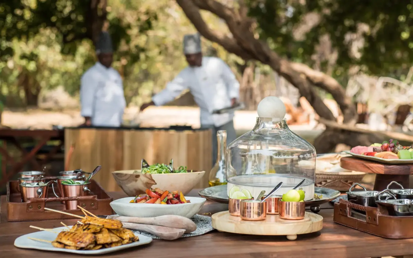 Outdoor dining setup with plated food and staff preparing meals, Chikwenya Camp, Mana Pools, Zimbabwe
