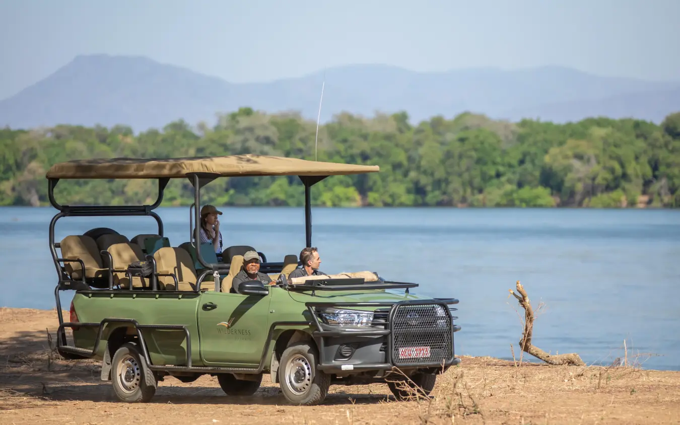 Safari vehicle with guests overlooking river and forested landscape, Chikwenya Camp, Mana Pools, Zimbabwe