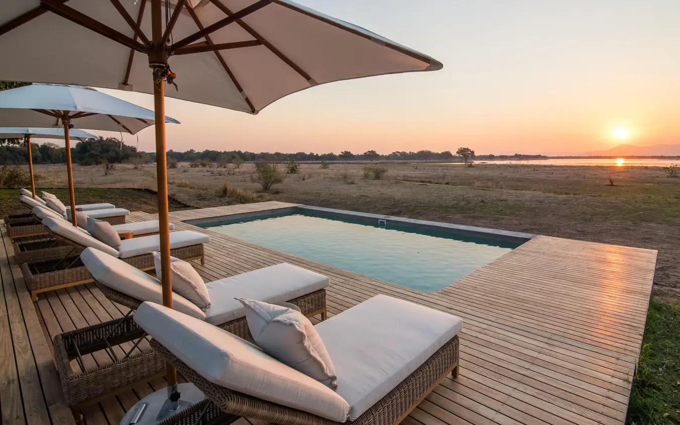 Wooden deck pool with loungers overlooking savanna at sunset, Chikwenya Camp, Mana Pools, Zimbabwe