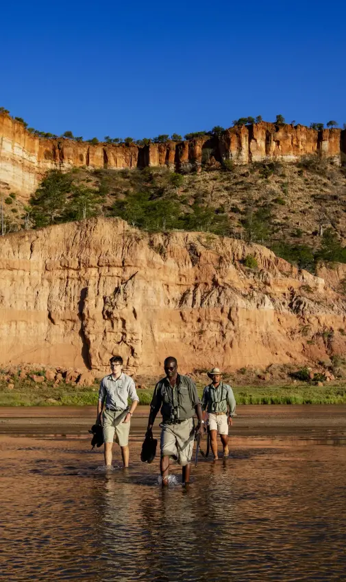 Guests wading in river beside towering sandstone cliffs, Gonarezhou & Malilangwe, Zimbabwe